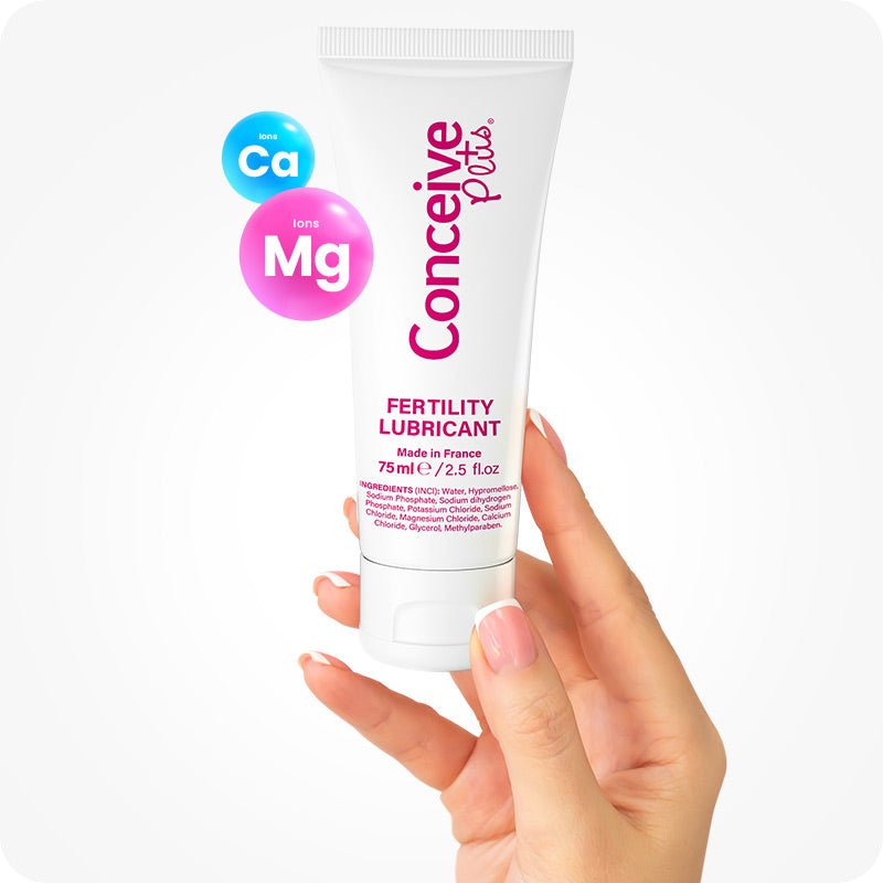 Conceive Plus Fertility Lubricant Combo featuring a 75ml fertility lubricant tube held upright by a hand with manicured nails, highlighted with calcium (Ca) and magnesium (Mg) ion graphics, against a bright white background.