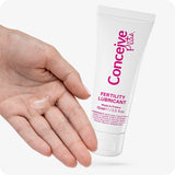 Conceive Plus Fertility Lubricant Tube 75ml held beside an open palm showing a clear portion of lubricant gel, demonstrating texture and product usage for fertility support.